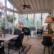 a farmhouse screened patio with benches, chairs and a dining set, table lamps, potted greenery and lanterns on the walls