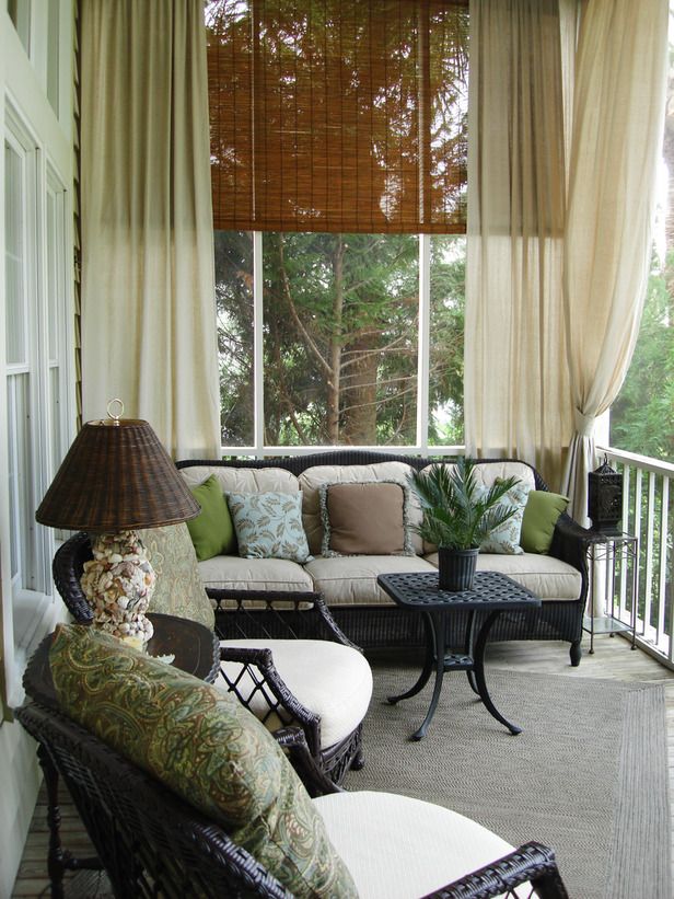 a screened porch with dark stained furniture, neutral upholstery, table lamps and greenery is a lovely nook