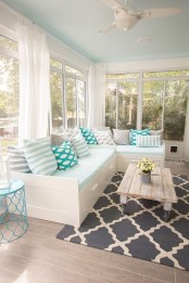 a modern neutral screened porch with a white corner sofa with storage, a printed rug, a whitewashed coffee table on casters and blooms in a jug