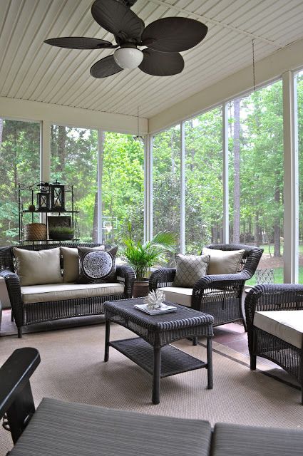 a modern screened porch with dark wicker furniture, neutral upholstery, potted greenery and lovely greenery around it