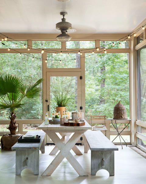 a relaxed boho screened porch with a whitewashed dining set, potted plants, string lights and a basket