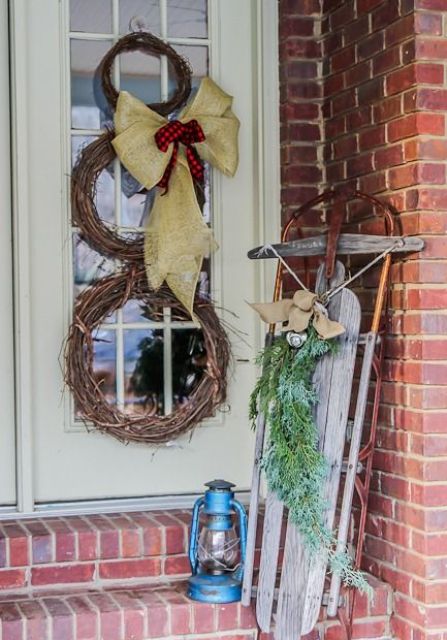 a snowman made of vine wreaths, with a burlap and plaid bow, a vintage sleigh with a burlap bow and fir branches plus a blue lantern for a rustic feel