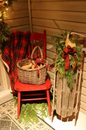 a red chair with a red plaid blanket, a basket with pinecones and berries, a wooden sleigh with a plaid bow and fir branches
