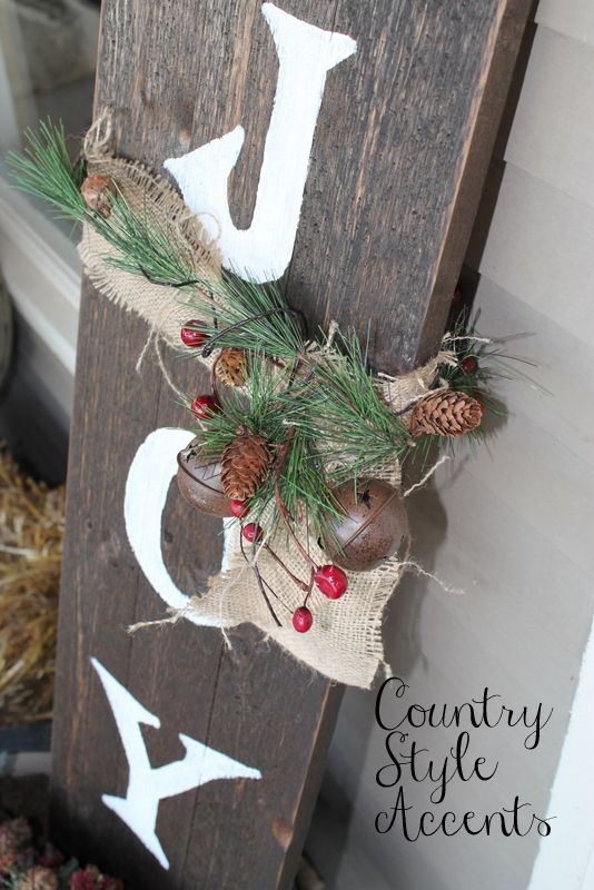 a wooden JOY sign with a burlap bow, fir branches, berries, bells and pinecones is a lovely and easy rustic decor idea
