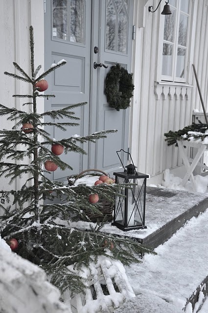 a Christmas tree with apples, a candle lantern and a fir branch wreath on the door for a natural feel in the porch