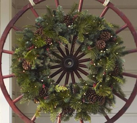 a wheel with a fir branch wreath, berries and lights for a cool rustic feel in your outdoor space