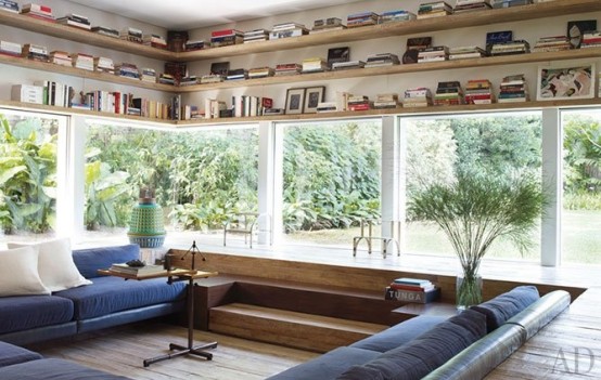 a modern living room with stained wood, a conversation pit with navy sofas,white pillows and potted plants is a lovely space with much natural light