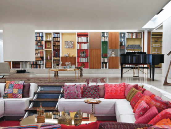 a bold modern living room with a built-in conversation pit with a white sofa, colorful and printed pillows, gold coffee tables that add chic and glam to the space