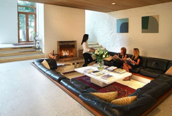 a modern conversation pit with a leather sofa that lines up the whole space and a coffee table and a fireplace opposite it