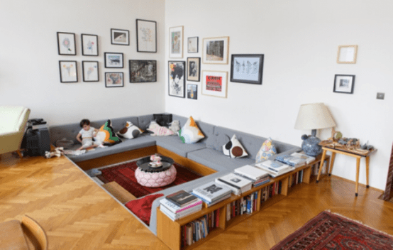 a mid-century modern living room with a conversation pit, a grey sofa, a bold rug and some bookshelves that separate this zone from the rest of the space