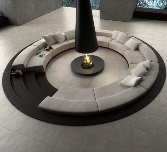 a neutral minimalist living room done with concrete, with a round conversation pit with an open fireplace in the center and a sofa all around it