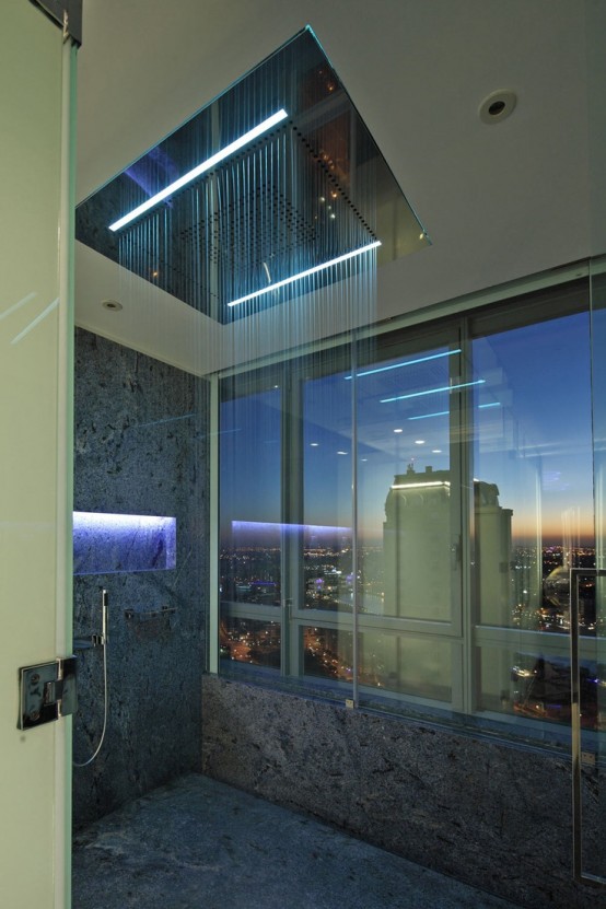 a gorgeous modern shower space with a view of the big city through a clear glass wall and built-in lights and a large rain shower
