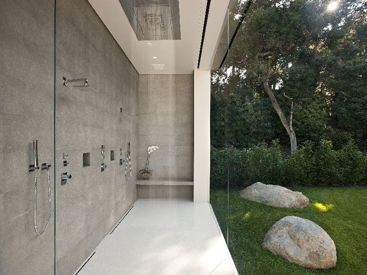 an indoor shower space done with concrete, with a clear glass wlal that lets the homeowners enjoy the views of their private garden
