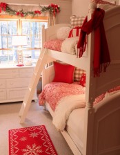 red and plaid festive bedding and a rug plus some garlands with red bows on the window for a cozy wintry feel in the space