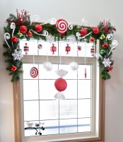 pretty and cute Christmas window decor with fir garlands, red and white ornaments, snowflakes and candies is a very cool idea for a kids’ room