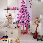 a white kids’ room with bright Christmas decor – a bright pink Christmas tree with colorful ornaments, bright ornaments on the mantel and bright flowers hanging down from the ceiling