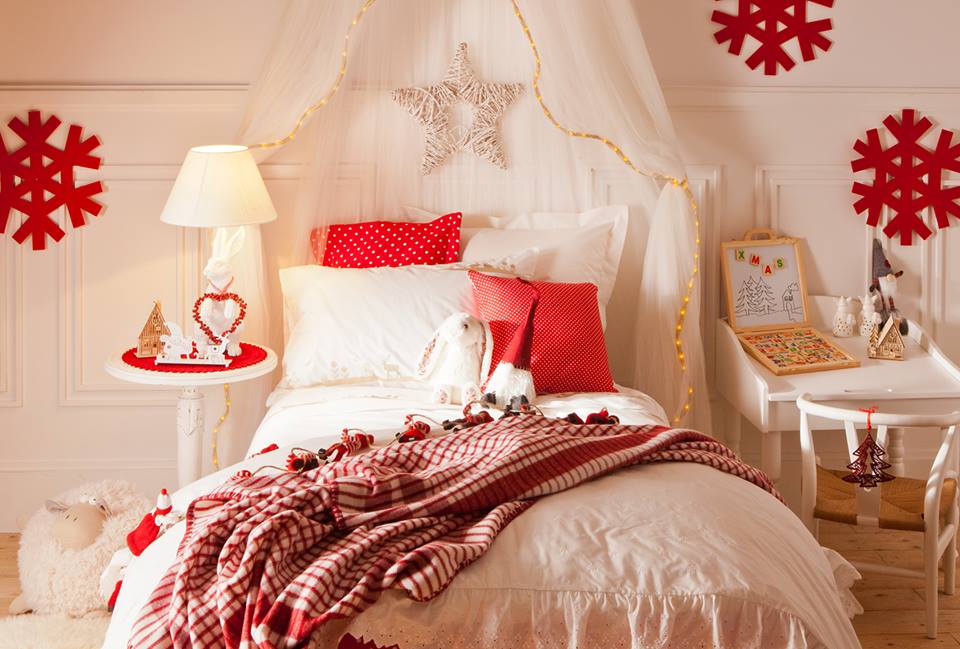 a beautiful neutral kid's room with chic red Christmas decor   red pillows, red snowflakes, blankets and mini nightstands plus a star on the bed is very cozy