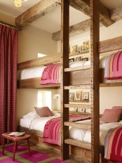 a cozy rustic kids’ room with four built-in bunk beds, with a ladder and pink and white bedding, with matching curtains and a rug