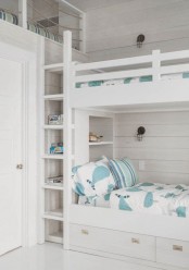 a white coastal bedroom with three built-in bunk beds, with pastel and white bedding, a ladder is a chic and lovely space that welcomes in