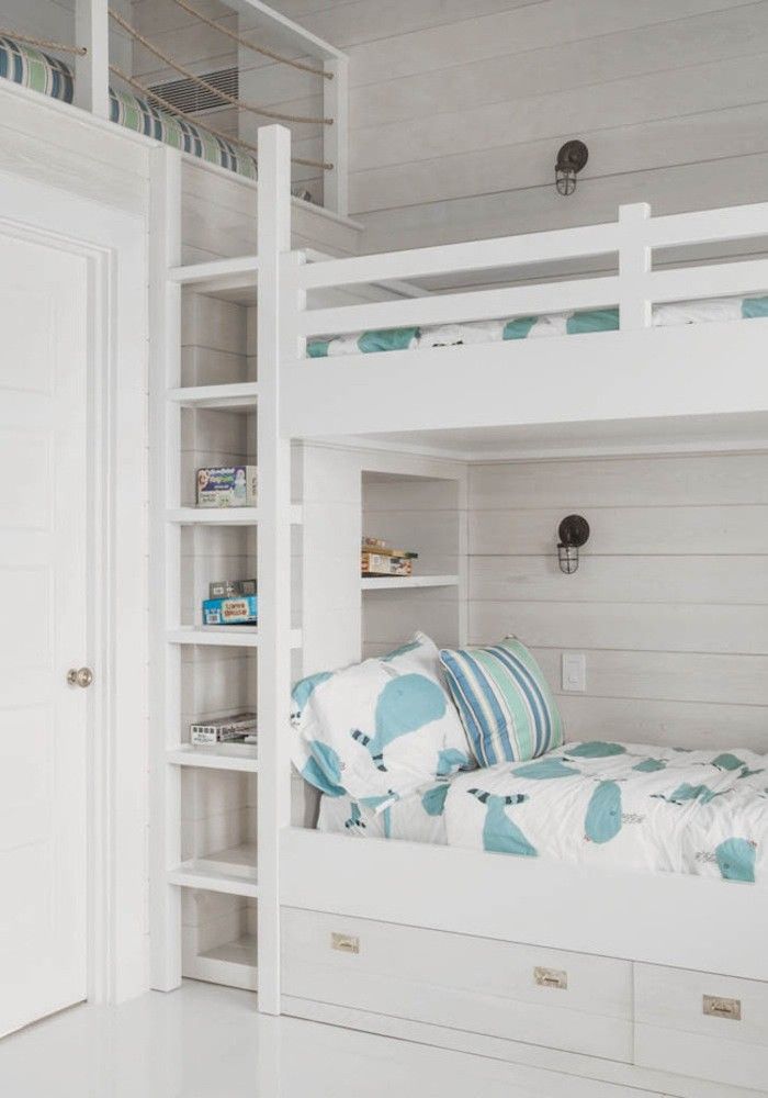a white coastal bedroom with three built in bunk beds, with pastel and white bedding, a ladder is a chic and lovely space that welcomes in