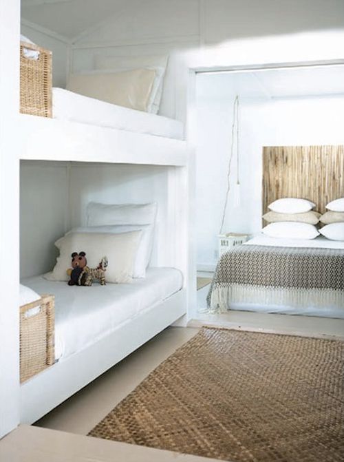 a neutral room with a large bed with neutral bedding, built-in bunk beds with white and neutral bedding, baskets for storage is an airy and chic space