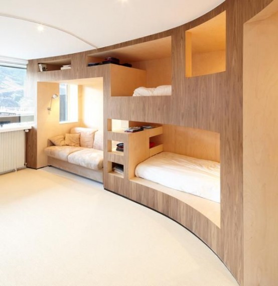 a rounded room with a large plywood unit that includes two bunk beds, storage units and a sofa by the window is a very welcoming and minimal space