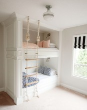 a small white nook with built-in bunk beds, with a rope ladder and a window with a black and white curtain is a lovely space
