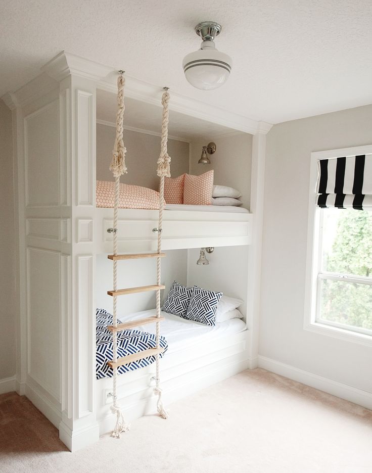 a small white nook with built in bunk beds, with a rope ladder and a window with a black and white curtain is a lovely space