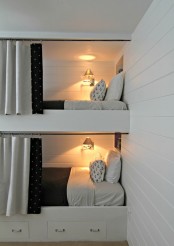 a white kids’ room with built-in bunk beds, black and white bedding and curtains, sconces on the walls for more coziness