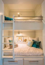a small white nook clad with shiplap, with built-in bunk beds, with neutral bedding and bright pillows plus built-in lights to make the sleeping space more welcoming