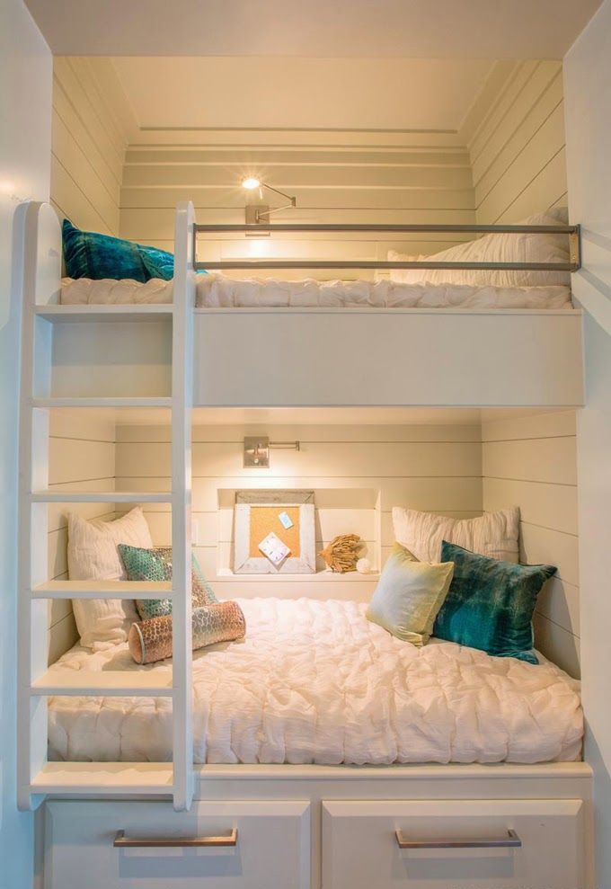 a small white nook clad with shiplap, with built in bunk beds, with neutral bedding and bright pillows plus built in lights to make the sleeping space more welcoming