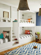 a bright kids’ room with navy and white walls, white built-in bunk beds, striped bedding and a printed rug is a cool space