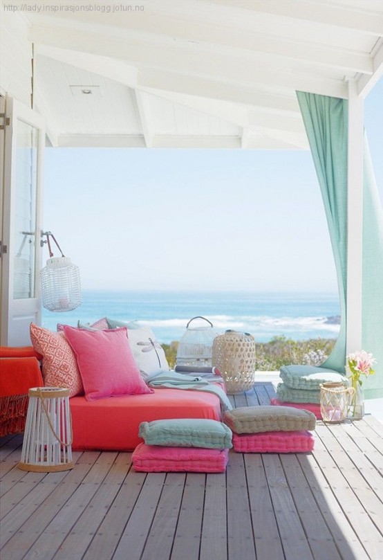 a colorful summer seaside terrace with a bright daybed, colorful pillows and cushions and candle lanterns