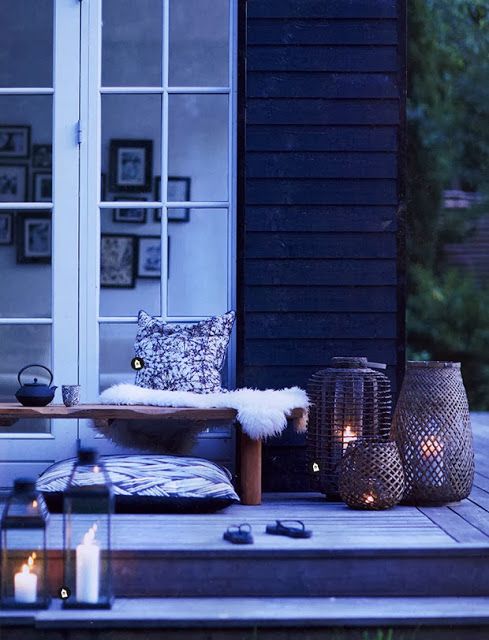 a Nordic summer terrace in black and white, with a bench, faux fur, pillows, wicker and glass candle holders