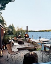a riverside deck with wicker chairs, a fireplace, candle lanterns, stump tables and a cool riverside view