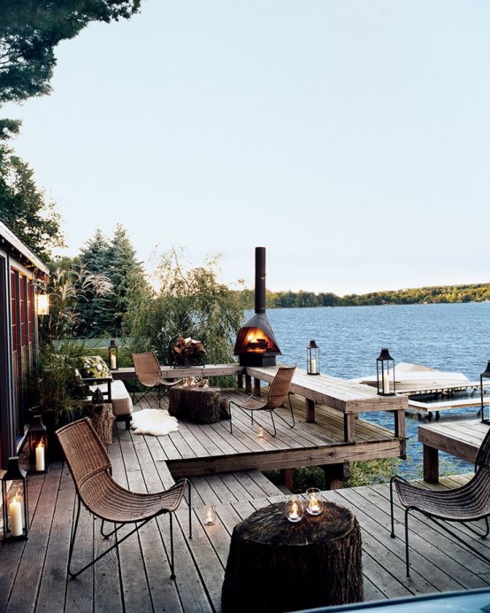 a riverside deck with wicker chairs, a fireplace, candle lanterns, stump tables and a cool riverside view