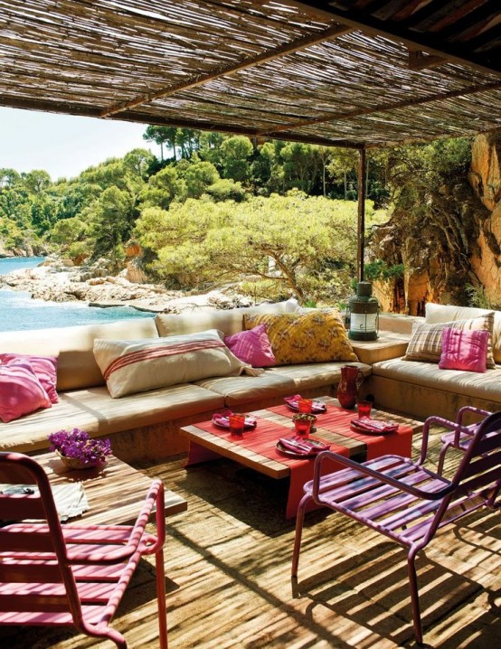 a bright and colorful terrace with neutral upholstered benches, colorful pillows, bright stools and textiles plus a sea view