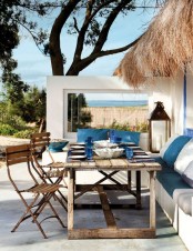 a bright summer seaside terrace with a built-in bench, wooden furniture, white and navy textiles, statement candle lanterns