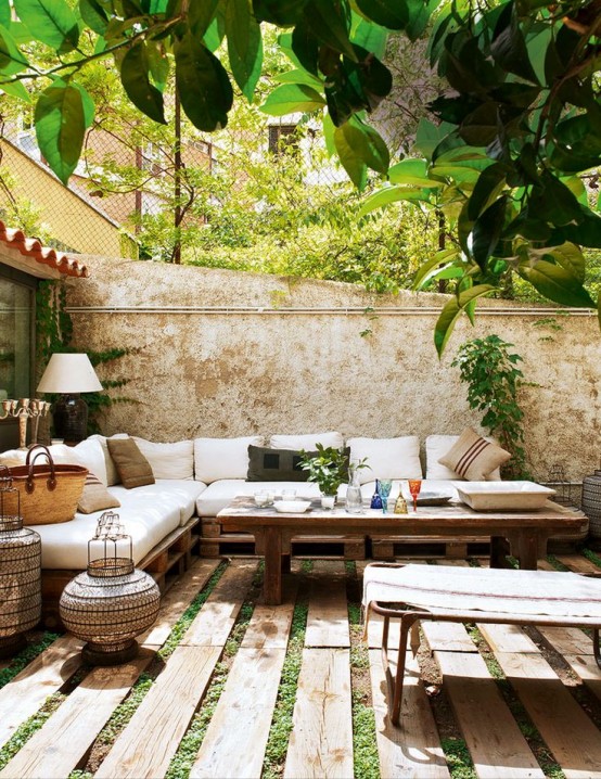 a welcoming Mediterranean summer terrace with pallet and rattan furniture, neutral upholstery and textiles, candle lanterns and greenery