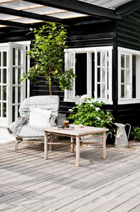 a summer Nordic terrace with rattan furniture, cozy neutral upholstery, potted greenery and a large tree