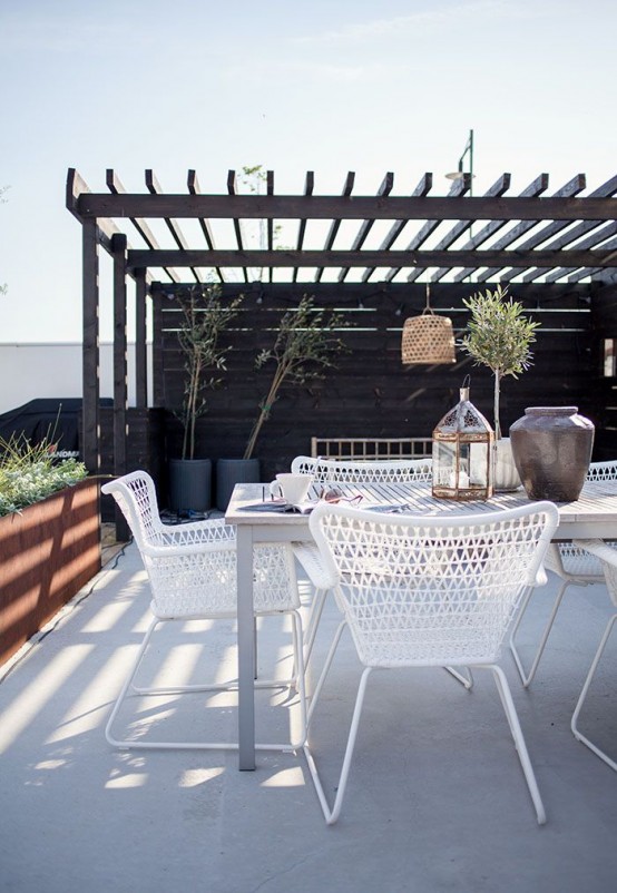 a monochromatic summer terrace with potted greenery and trees, white furniture of metal and wood, candle lanterns