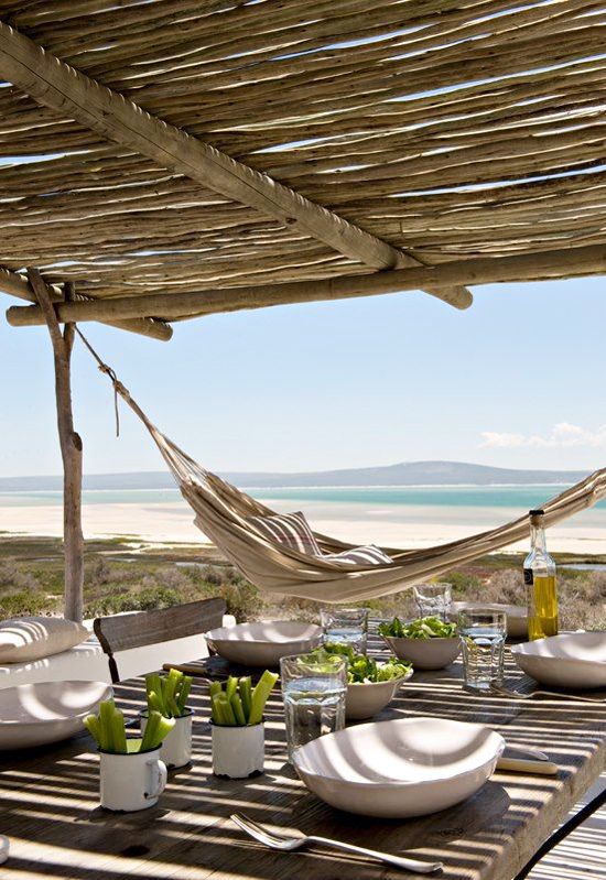 a cheerful island summer terrace made of wood, with neutral textiles and a cool dining zone plus a gorgeous sea view
