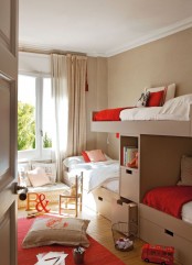 a greige kids’ room with four bunk beds, a cushion with pillows on the floor and some bright red touches here and there