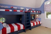 a seaside kids’ room with navy built-in bunk beds and bright bedding, porthole windows and bright curtains