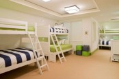 a large neutral kids’ room with three bunk beds in white, with navy, white and green bedding and lights on the ceiling