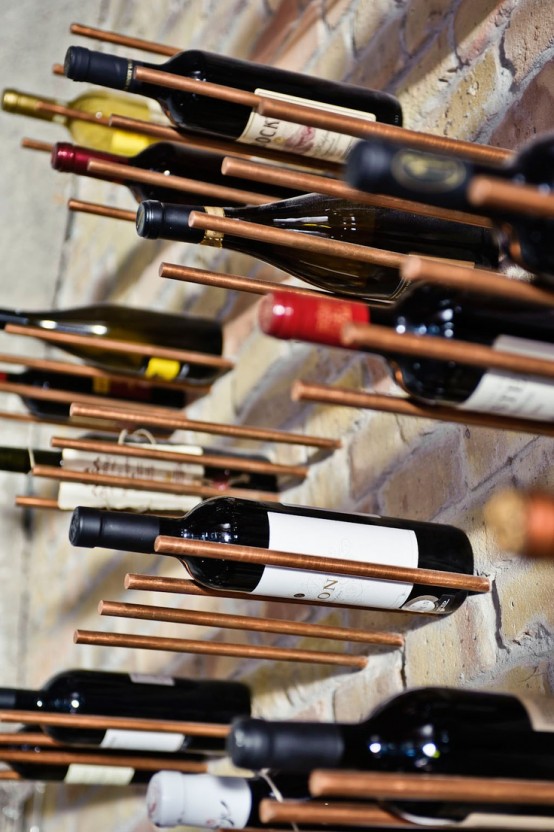 a brick wall with copper metal dowels that are used to hold wine bottles for an industrial kitchen