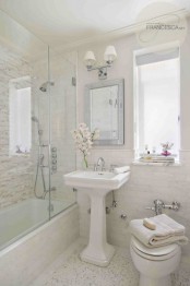 a neutral bathroom done with three kinds of tiles, a tub with a shower space in one, a free-standing sink and elegant lamps