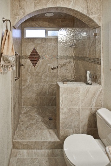 a neutral stone tile bathroom with an arched shower space and a tiny window for more natural light