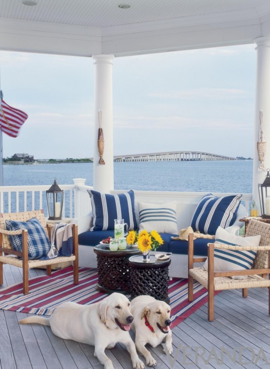 a beachy patio with woven and white wooden furniture, striped navy and white textiles, dark coffee tables, a striped rug and a cool view