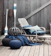 a seaside patio of wood and with a rattan lounger, with blue textiles, crochet ottomans and oars is very cozy